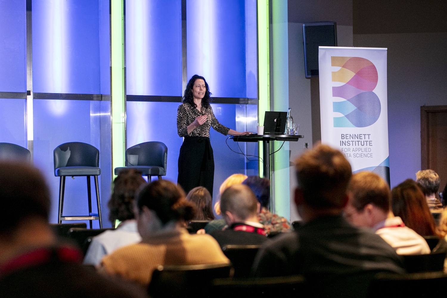Catherine Stables presenting on stage, next to a human-sized banner of
the Bennett logo
